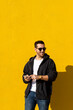 © Cavan Images - Bearded man with sunglasses standing against yellow wall, using phone