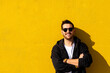 © Cavan Images - Young bearded man standing against a yellow wall with crossed arms