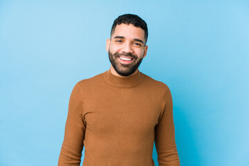 young latin man against a blue background isolated happy, smiling and cheerful.