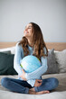 © BestForYou - Woman is planning a trip, hugging globe sitting on the couch.