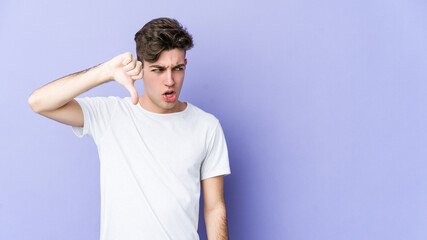 Wall Mural - Young caucasian man isolated on purple background showing thumb down and expressing dislike.