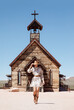© Ania Boniecka/Stocksy - Stylish cowgirl walks in front of old church in the desert.