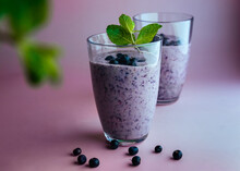 Two Glasses Of Homemade Smoothie With Fresh Blueberries With Mint Leaves On Pastel Pink Background.