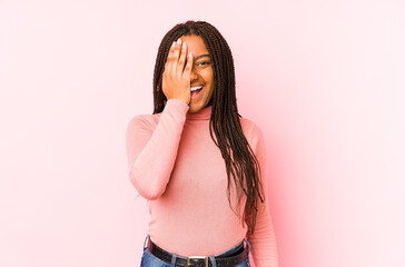 Young african american woman isolated on a pink background having fun covering half of face with palm.