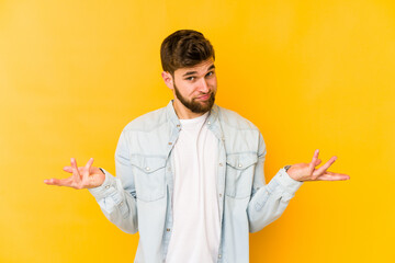 Wall Mural - Young caucasian man isolated on yellow background doubting and shrugging shoulders in questioning gesture.