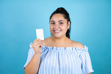 Young beautiful woman with curly hair over isolated blue background smiling and showing white card