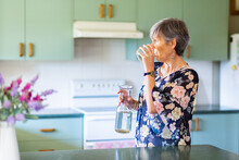 Woman Drinking A Glass Of Water In Her Kitchen