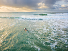 Looking Down On A Lone Surfer Paddling Into Waves Under A Darkening Sky