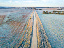 A Dirt Road Leading Off To The Horizon Between Frost Covered Paddocks