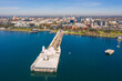 © Gary Chapman/Austockphoto - Aerial view of a long straight jetty with buildings on the end and a coastal city in the background