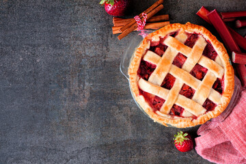 Poster - Strawberry rhubarb pie. Overhead view corner border against a dark stone background with copy space. Autumn food concept.