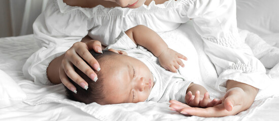 Portrait of enjoy happy love family asian mother playing with adorable little asian baby.Mom kiss with cute son moments good time in a white bedroom.Love of family concept