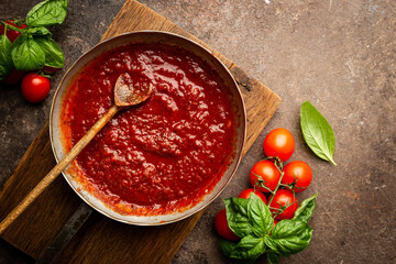 Wall Mural - Classic homemade Italian tomato sauce with basil for pasta and pizza in the pan on a wooden chopping board on brown background, top view.