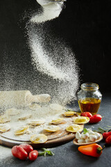 Wall Mural - The flour falls on the ravioli. Delicious raw ravioli with cheese and flour, cherry tomatoes, sunflower oil and basil on a dark background