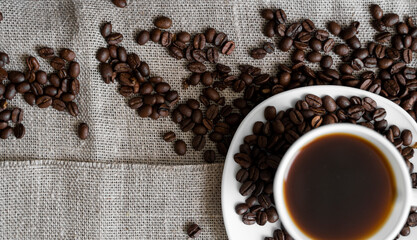 Coffee cup with roasted coffee beans on linen background. Mug of black coffe with scattered coffee beans. Fresh coffee beans.