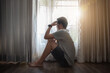 © NINENII - Sad and depressed young male sitting on the floor in the living room looking outside the doors,sad mood,feel tired, lonely and unhappy concept. Selective focus.