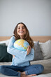 © BestForYou - Cheerful young woman hugging globe sitting on the couch at home.
