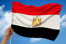 Male Hand Holds Against The Background Of The Sky With Clouds The National Flag Of Egypt On A Luxurious Texture Of Satin, Silk With Waves, Close Up, Copy Space, Concept Of Travel, Economy, Politics