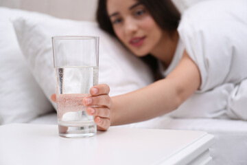 Wall Mural - Young woman taking glass of water from nightstand at home, focus on hand