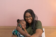 © tampatra - Portrait of smiling business black African american woman, a mom with her daughter working from home in family relationship concept on pink background. A black kid toddler girl with her parent.