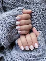 Beautiful well-groomed female hands with French manicure on a gray knitted background.  Fashionable color of nail gel polish.  Beauty salon concept.