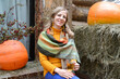 Happy woman with a mug of tea in her hand sits against the background of orange pumpkins in the courtyard of a rural house. Portrait