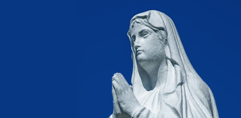 Fototapete - Close up ancient statue of the Virgin Mary praying against blue background of sky
