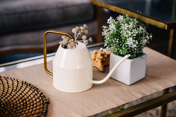 Flowers in a pot and a decorative teapot on the table, the interior of the apartment