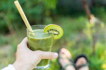 Woman hold healthy fresh natural green smoothie in glass with  bamboo juice straw. Made from spinach, apple, kiwi, avocado, bananas. Detox day.
