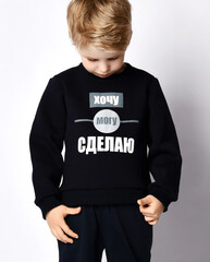 Wall Mural - Closeup of blond kid boy in black jersey sweater reading printed words inscription on it. Translation: 