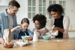 © fizkes - Happy interested multiethnic small children girls in aprons involved in preparing dough for homemade pastry with affectionate loving african american mommy and european father in modern kitchen....