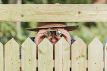 Curious Neighbor Stands Behind A Fence And Watches With Binoculars