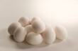 Weiße Eier gestapelt auf einem Haufen im warmen Gegenlicht auf einem neutralen warm-weißen Hintergrund