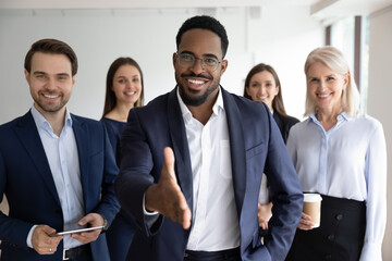 Wall Mural - Portrait of smiling African American team leader stretch hand greeting job candidate or applicant in office. Happy multiracial businesspeople meet welcome newcomer at workplace. Employment concept.