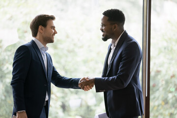 Wall Mural - Smiling multiracial businessmen shake hands get acquainted greeting at meeting in office. Happy diverse male colleagues or business partners handshake close deal make agreement. Partnership concept.