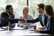 Smiling diverse businesspeople shake hands get acquainted greeting at team meeting in office. Happy multiracial male colleagues employees handshake at briefing with coworkers. Acquaintance concept.