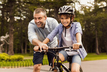 Boy Learning How To Ride Bicycle With His Happy Dad