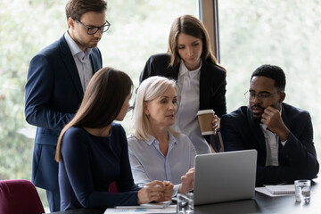 Poster - Concentrated multiracial businesspeople brainstorm look at laptop screen discussing company business project together. Focused diverse colleagues talk cooperate on computer at team meeting in office.