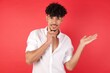 © Roquillo - Funny Young arab man with afro hair wearing shirt standing over isolated red background hold open palm new product great proposition