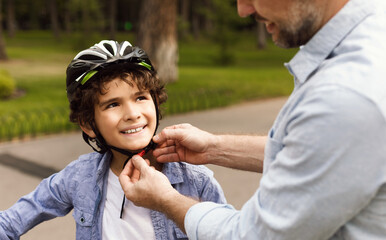 Adult man putting safety helmet on his son