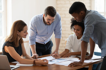 Wall Mural - Smiling diverse multiethnic businesspeople discuss documents paperwork statistics at meeting in office together, focused multiracial colleagues negotiate consider paper financial reports at briefing