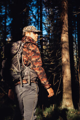 Hiker hiking in autumn forest. Male hiker in camouflage jacket with backpack looking to the side walking in forest. Caucasian handsome male outdoors in nature. Concept of forest wear, navigation.