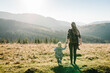 © Serhii - Mom with backpack and child walk in autumn grass. The daughter and mother walking on nature. Family spending time together in mountain on vacation. Holiday trip concept. World Tourism Day. Back view.