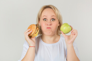 beautiful young plump woman in a white t-shirt on a white background with a burger and an apple