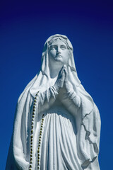 Antique white statue of the Virgin Mary praying on blue background.