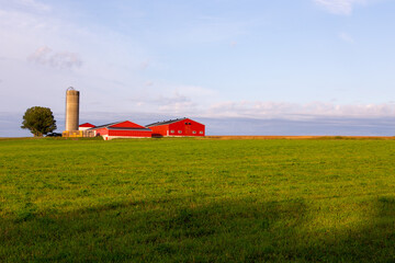 Horizontal view of a St. François village farm with bright orange buildings and tall silo seen during a summer morning, Island of Orleans, Quebec, Canada