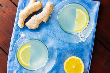 Wall Mural - Ginger tea with lemon on a blue napkin. Two cups of ginger tea with lemon on wooden background. Top view