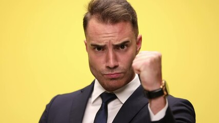 Poster - close up of a handsome businessman rising firmly his fist, pointing at camera, and gesturing a beat up sign on yellow background