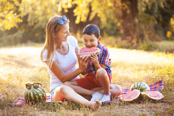 happy smiling kid with mom eating ripe watermelon in summer park