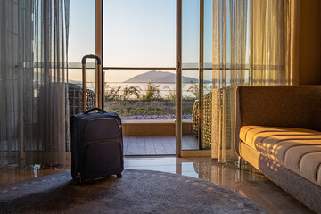 travel bag suitcase luggage in front of window in luxury hotel room with seaview on sunrise